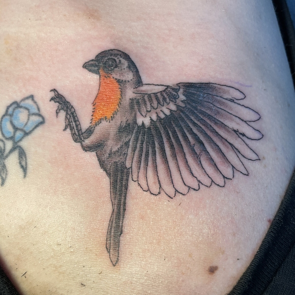 A flying bird ltattoo ands on a flower on the shoulder